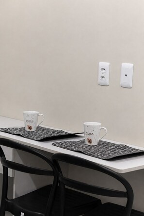 A conference table with two white mugs on black placemats, a black chair, and two electrical outlets on the wall. - Fully furnished apartment, 5 min walk from UFMS (Federal University of Mato Grosso do Sul), near the University Hospital (HU). (Campo Grande)