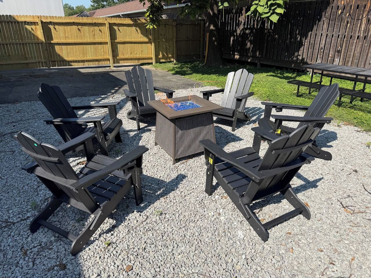 Un espace extérieur aménagé avec des fauteuils Adirondack, une table carrée et un foyer.