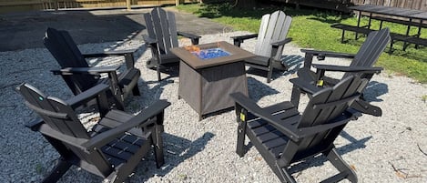 Un espace extérieur aménagé avec des fauteuils Adirondack, une table carrée et un foyer.