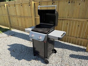 A portable gas grill with two control knobs, a side shelf, and a foldable table. - Highlands Gateway | Games, Fire Pit, 4BR Fun (Louisville)
