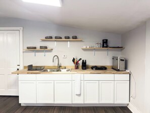 A modern kitchen with white cabinetry, a wooden countertop, and built-in shelves above the sink. - Highlands Gateway | Games, Fire Pit, 4BR Fun (Louisville)