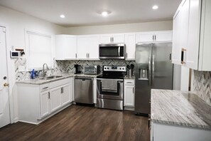 A modern kitchen with white cabinets, stainless steel appliances, and a herringbone tile backsplash. - Suite 1275 (East Point)