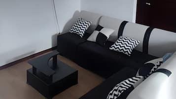 Een moderne woonkamer met een flatscreen televisie aan de muur, een zwart-wit bank en een donkerhouten deur.