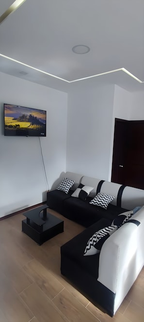A modern living room with a flat-screen TV mounted on the wall, a black and white sofa, and a dark wooden door.