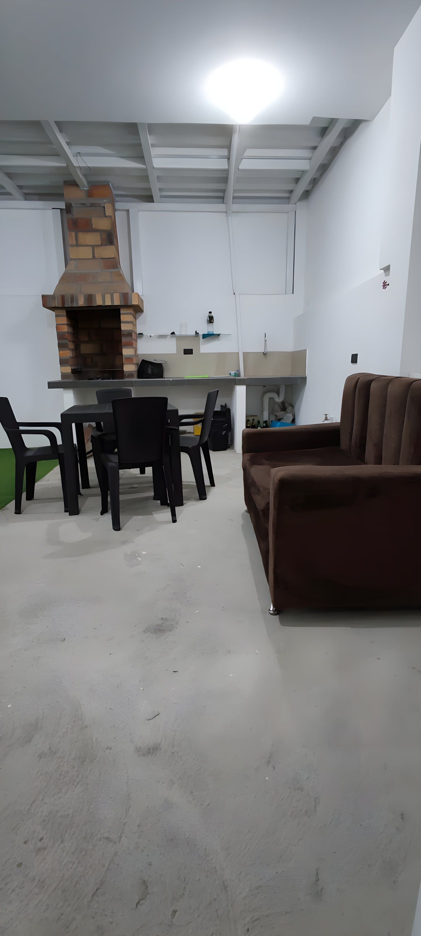 A room with a brick fireplace, a dining table with chairs, and a brown sofa.