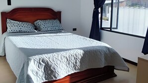 Une chambre à coucher avec un lit, une fenêtre avec des rideaux et un luminaire au plafond.
