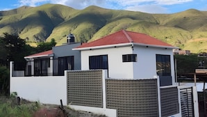 Une maison moderne à deux étages, avec un toit rouge, des murs blancs et une cour clôturée.