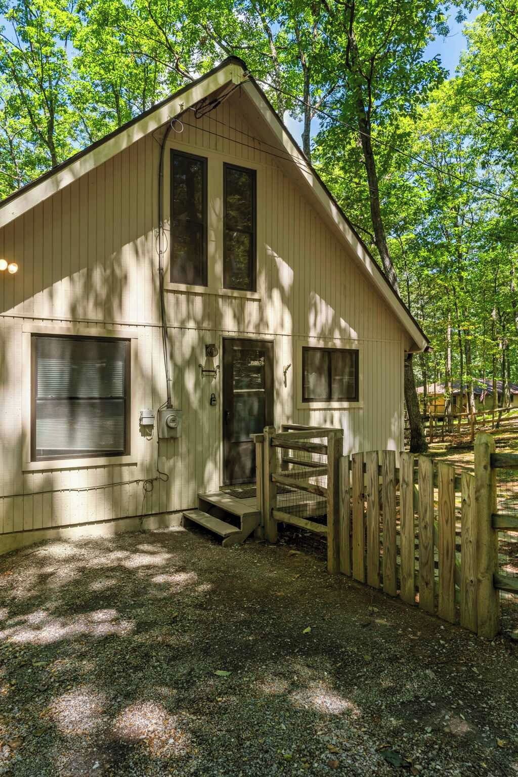 A two-story wooden cabin with a front porch and a fenced yard.