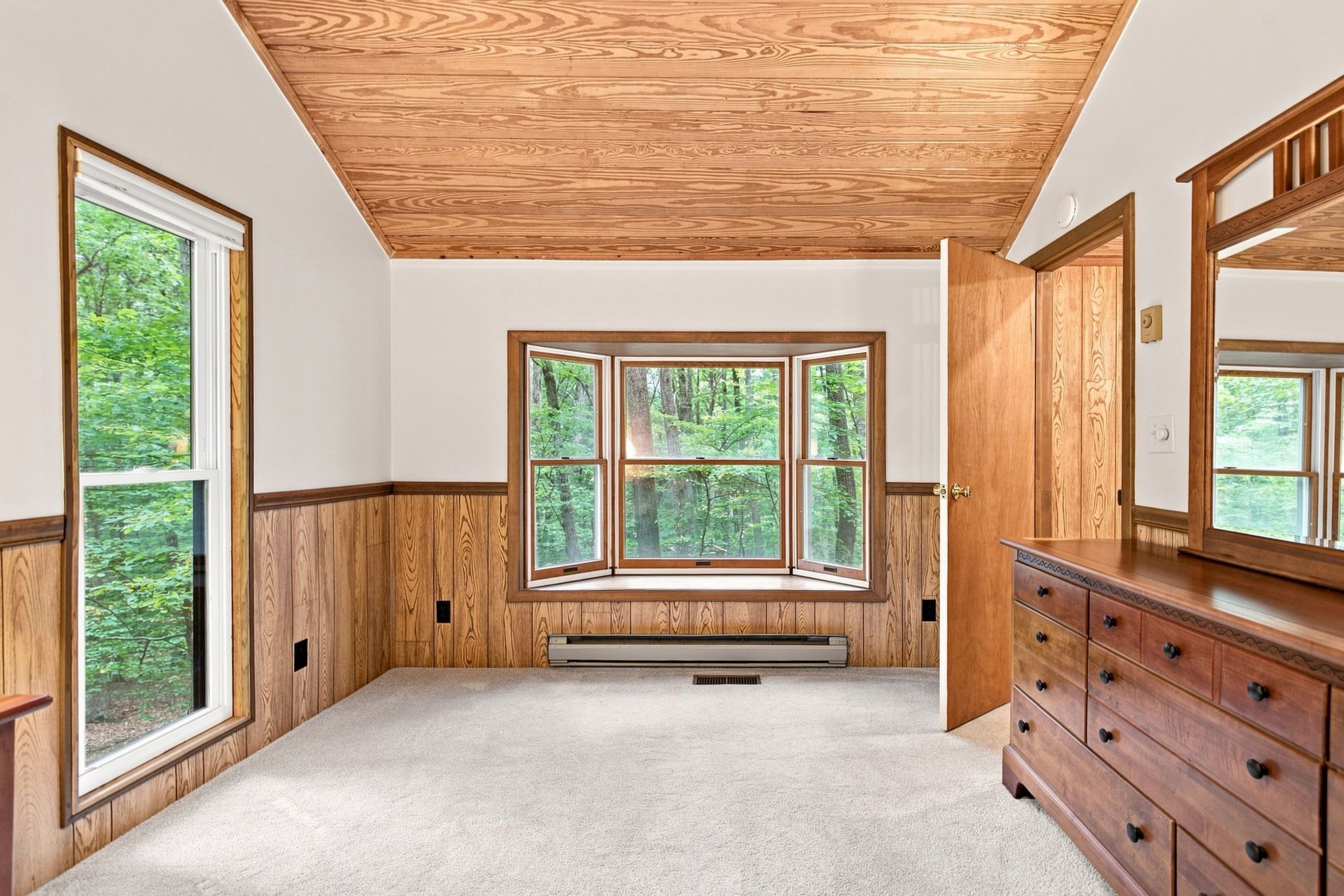 Una habitación con un amplio ventanal, paneles de madera, un calentador integrado y un aparador de madera.