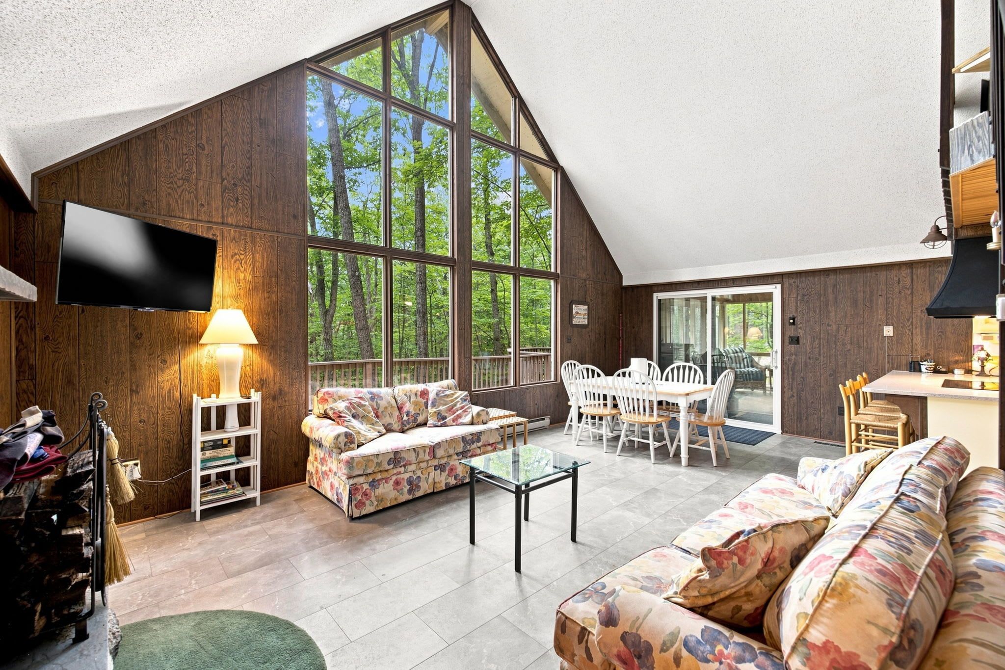 A spacious living area with a large window, a flat-screen TV, a sofa, a coffee table, and a dining table with chairs.
