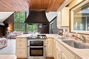 A modern kitchen with a large island, stainless steel appliances, and a view of the outdoors through large windows.