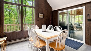 A dining area with a table and chairs, large windows with a view of trees, and a sliding glass door leading to an outdoor area. - Pet-Friendly with Treehouse, Deck in The Woods Resort (Hedgesville)