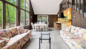 A spacious living area with a dining table and chairs, a sofa, and a kitchen area with a bar. - Pet-Friendly with Treehouse, Deck in The Woods Resort (Hedgesville)