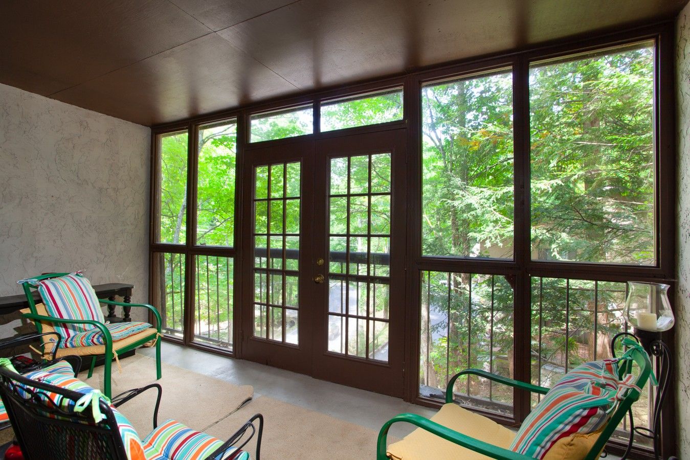 A room with large windows, a chair with a striped cushion, and a table.