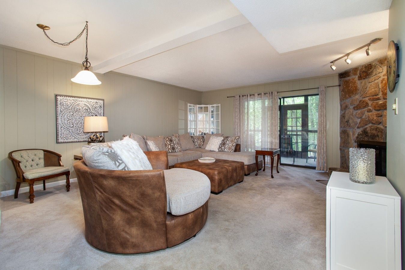 A spacious living room with a sectional sofa, a wooden chair, a lamp, and a stone fireplace.