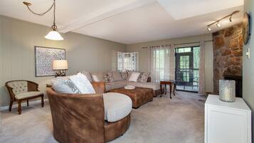 A spacious living room with a sectional sofa, a wooden chair, a lamp, and a stone fireplace.