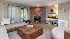 A living room with a stone fireplace, a sofa, a coffee table, and a television. - Smoky Laurel Cottage - Mountain Views & Fireplace! (Gatlinburg)