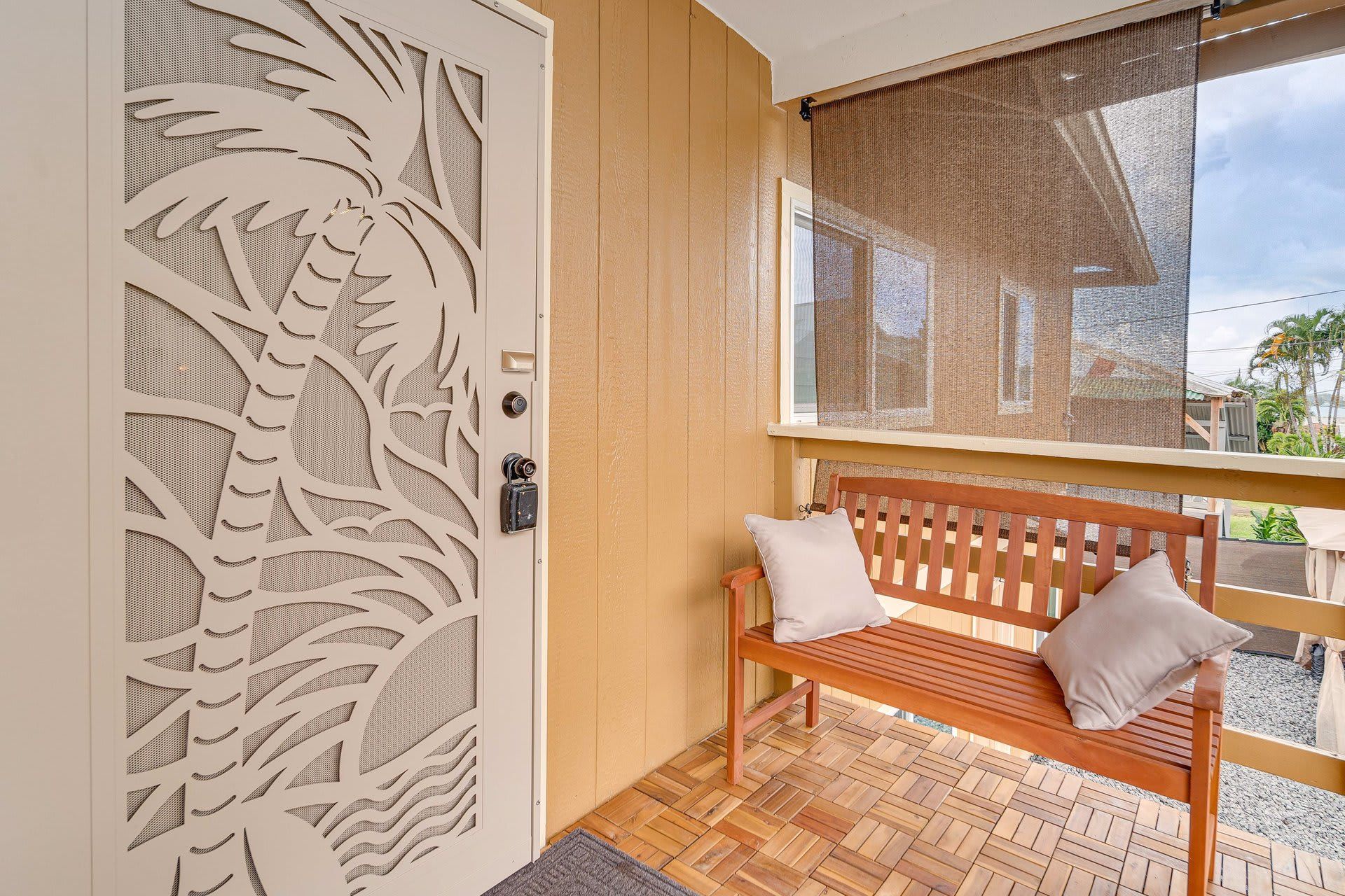 Um banco de madeira com almofadas, uma porta com detalhe decorativo recortado e uma janela com vista para o exterior.