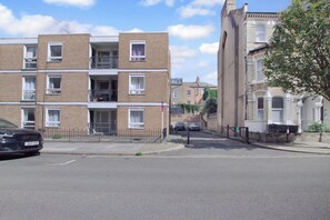A multi-story residential building with a brick facade, a gated entrance, and a parking area with cars. - Stylish 3BR Apartment | Clapham Junction | Parking (London)