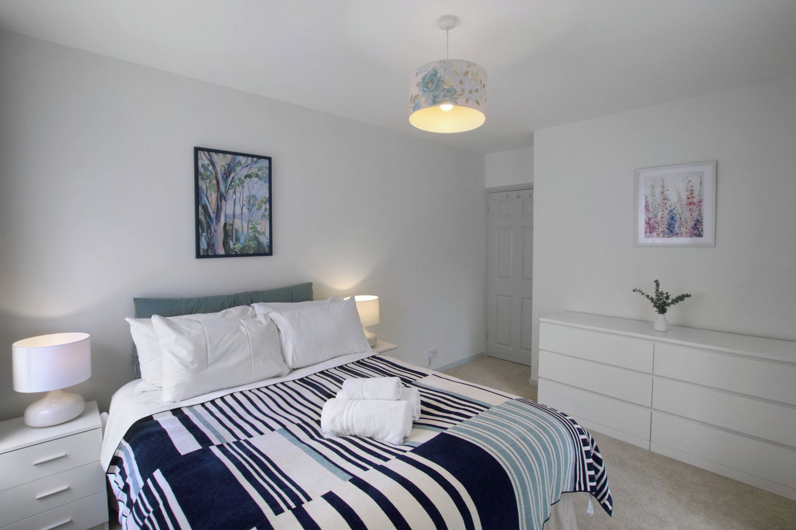 A bedroom with a bed, bedside lamps, a dresser, and wall art.