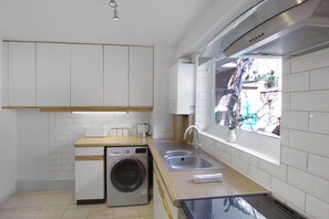 Eine moderne Küche mit weißen Schränken, einer eingebauten Waschmaschine, einem Spülbecken und einem Fenster mit Blick ins Freie.