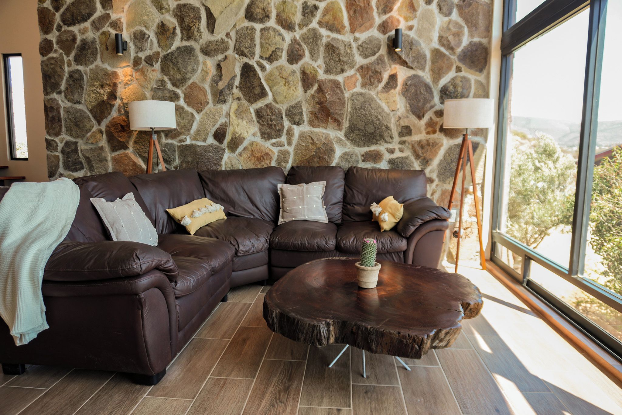 A modern living room with a stone wall, leather sofas, a round coffee table, and a view through a large window.