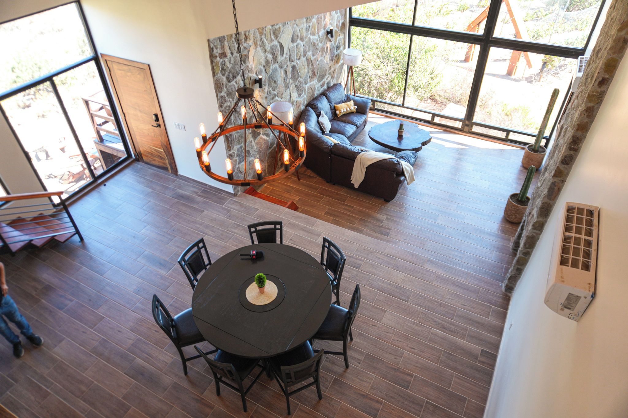 A spacious living area with a stone wall, a dark leather sofa, a round dining table with chairs, and a large window providing a view of the outdoors.