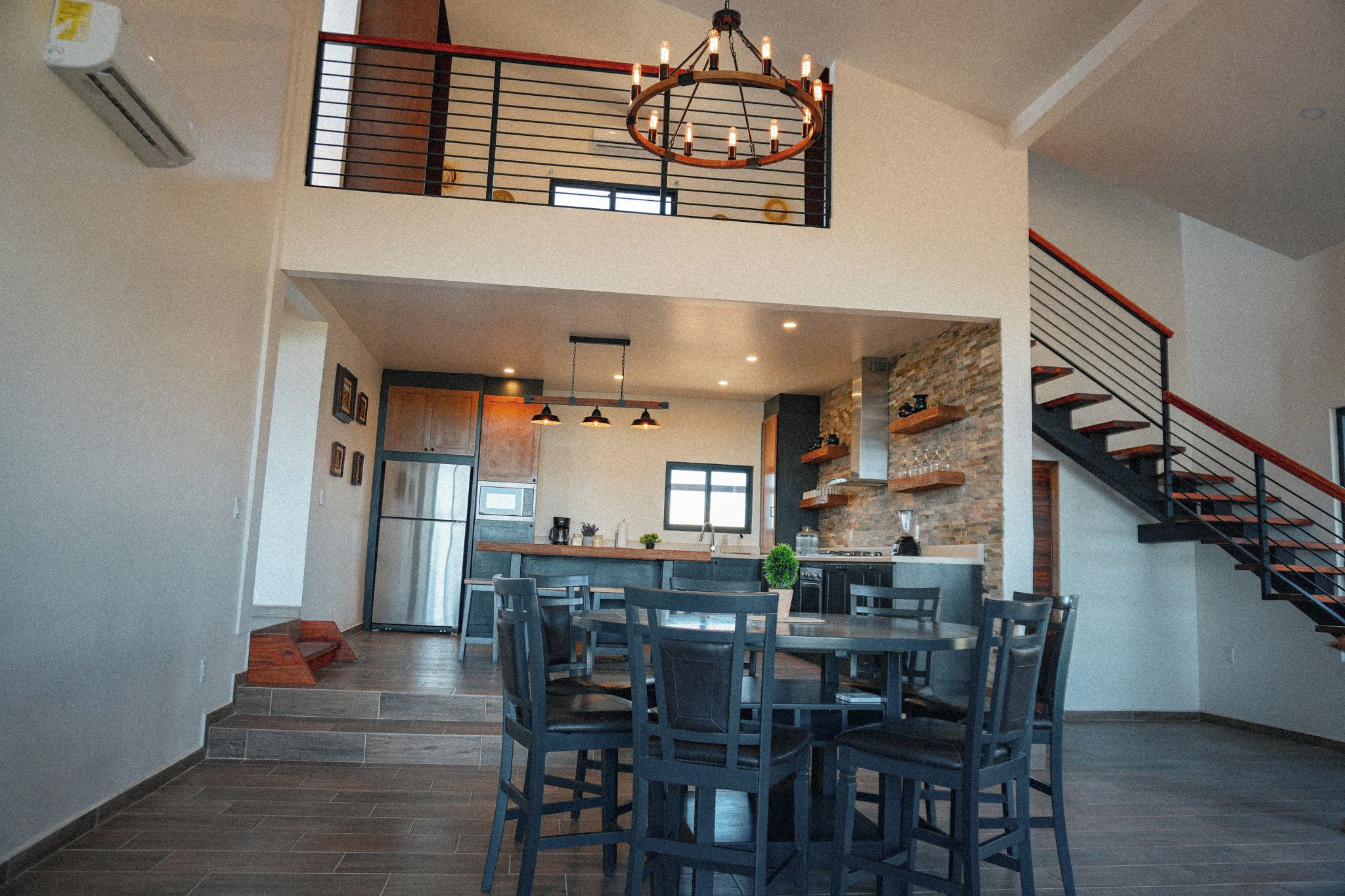 Une cuisine spacieuse dotée d’un îlot central, d’un coin repas avec des chaises, d’un escalier et d’un lustre.