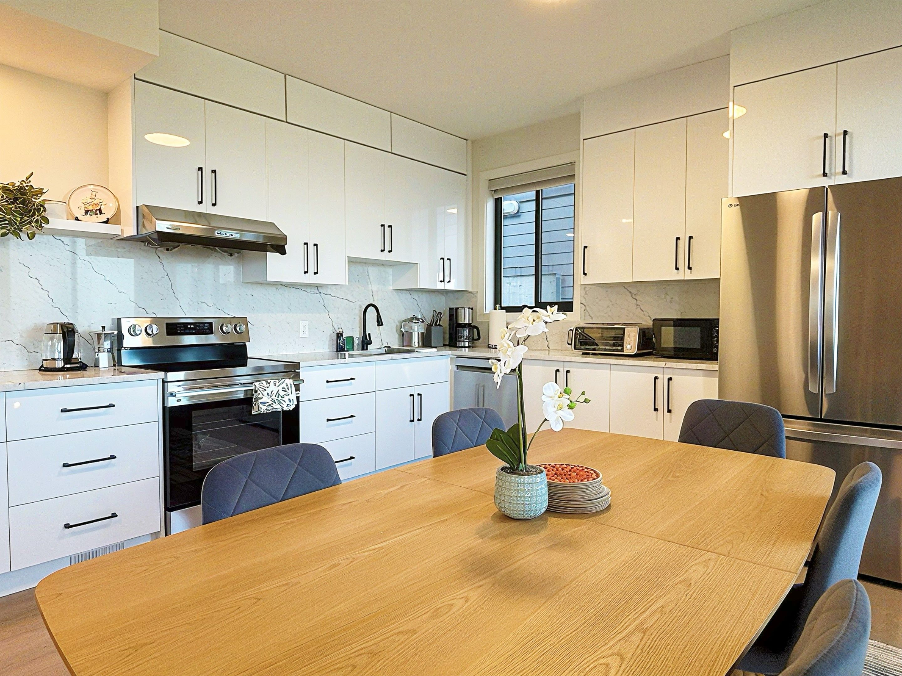 Una cocina moderna con gabinetes blancos, electrodomésticos de acero inoxidable y una mesa de comedor de madera.