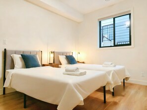 Une chambre d’hôtel avec deux lits, chacun doté d’une tête de lit, de tables de chevet et de lampes. Une fenêtre offre une vue sur un bâtiment situé à l’extérieur.