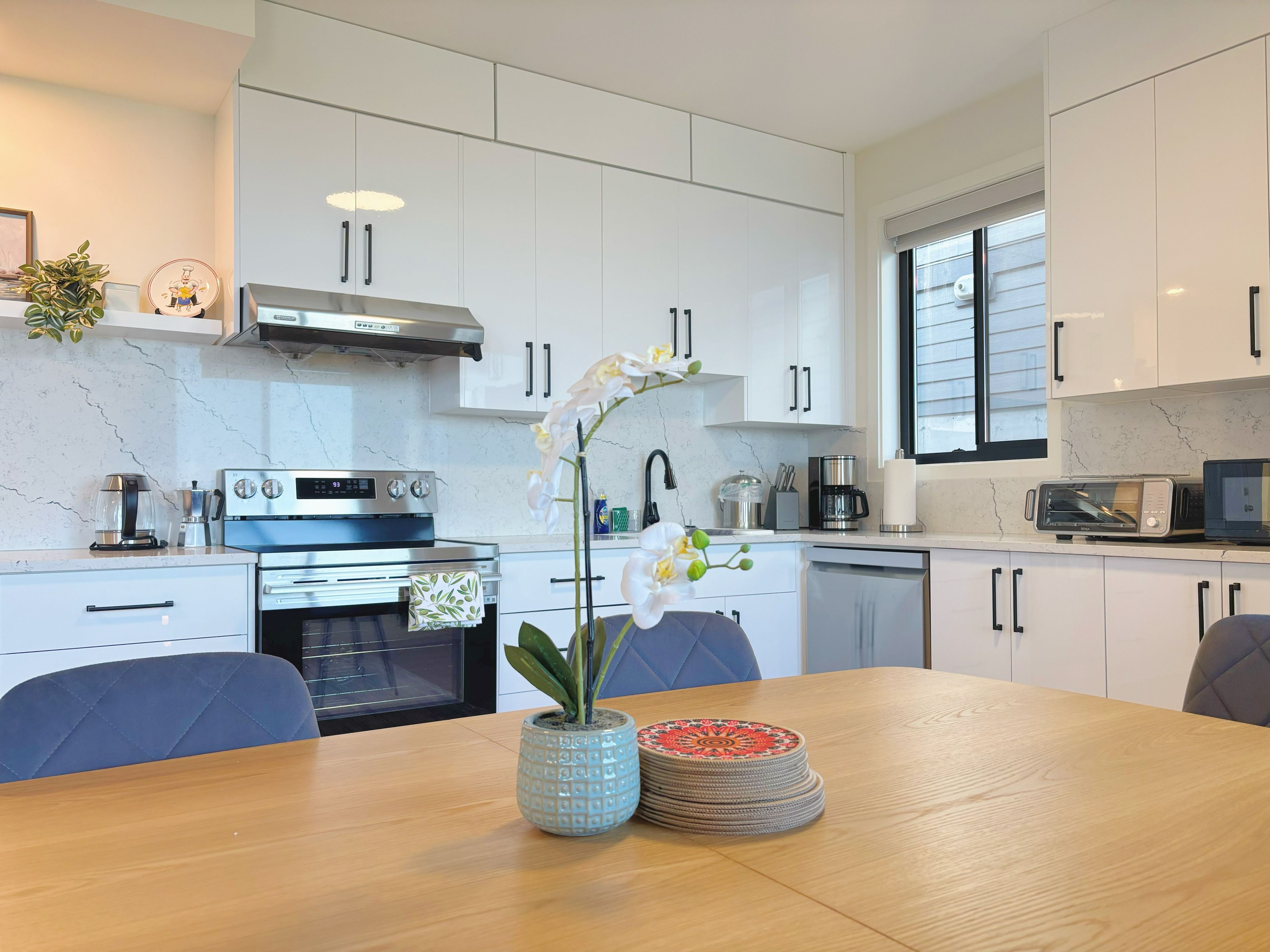 Una cocina moderna con armarios blancos, un horno de acero inoxidable y una mesa de comedor con sillas.