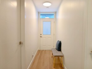 A narrow hallway with a white door at the end, a bench with a cushion, and a wooden floor. - Panoramic Ocean Views – 4-Bedroom North Nanaimo Suite with Private Balcony (Nanaimo)
