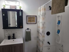 A bathroom with a mirror, a framed sign, a towel, a shower curtain, and toiletries.