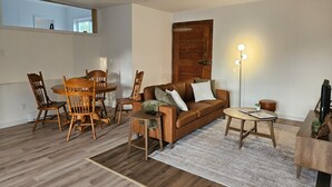 Una sala de estar con una mesa de comedor de madera, sillas, un sofá marrón, una lámpara de pie y una pequeña mesita auxiliar.