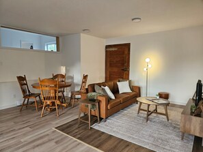 Een woonkamer met een houten eettafel, stoelen, een bruine bank, een vloerlamp en een klein bijzettafeltje.