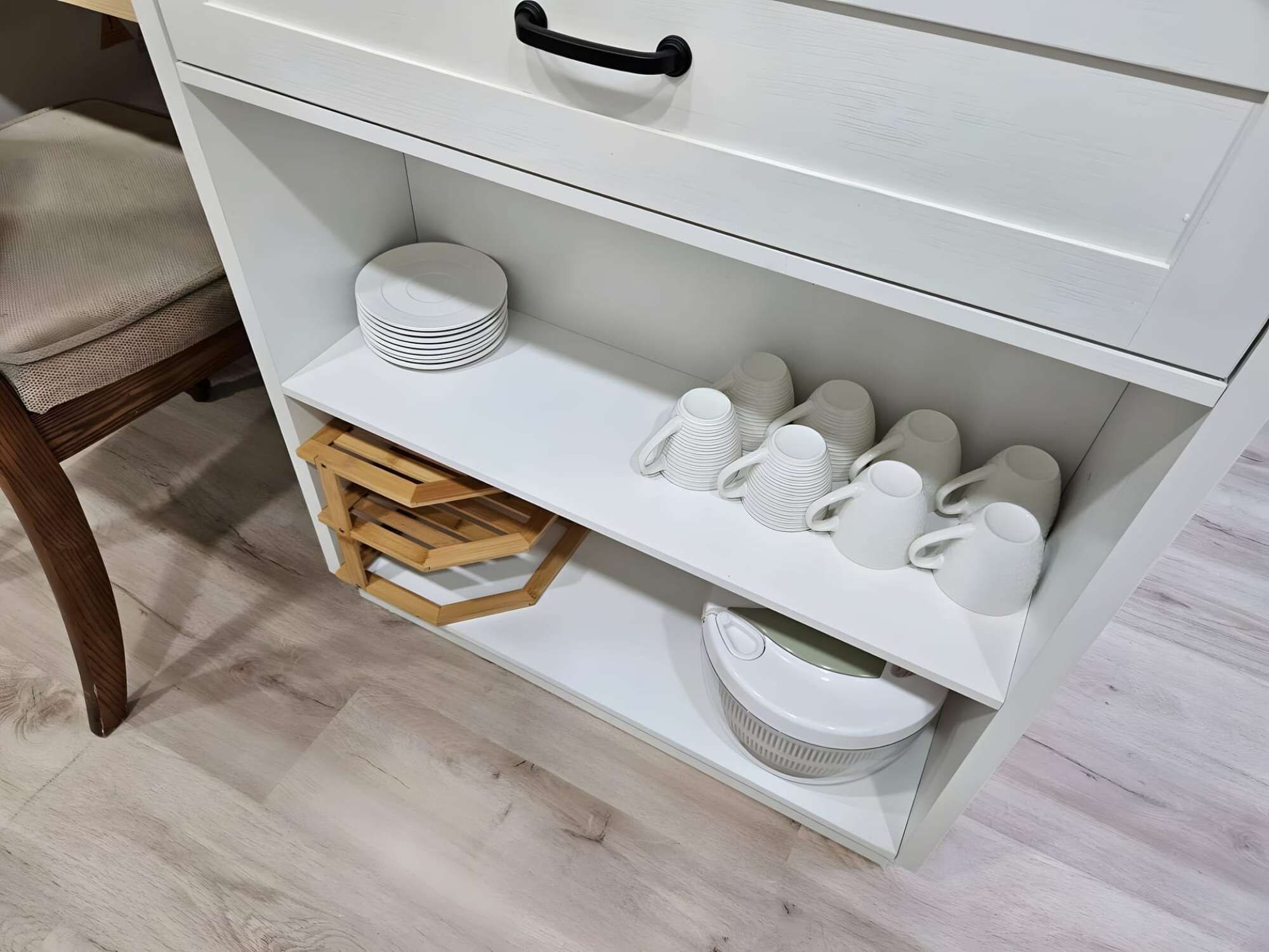 Un depósito blanco con estantes que contienen platos, tazas y un taburete de madera.