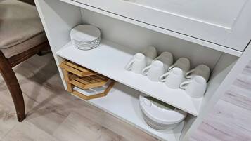 Un depósito blanco con estantes que contienen platos, tazas y un taburete de madera.
