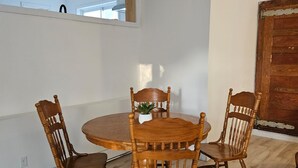 Un comedor con una mesa redonda de madera y cuatro sillas, una planta pequeña en maceta y una puerta de madera.