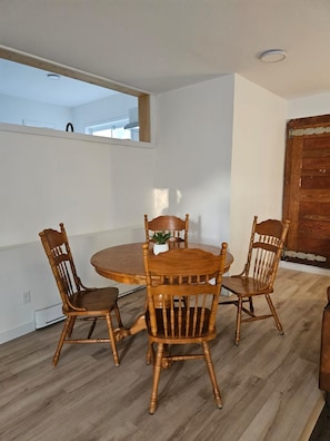 Een eetgedeelte met een ronde houten tafel, vier stoelen, een kleine pot met een plant en een houten deur.