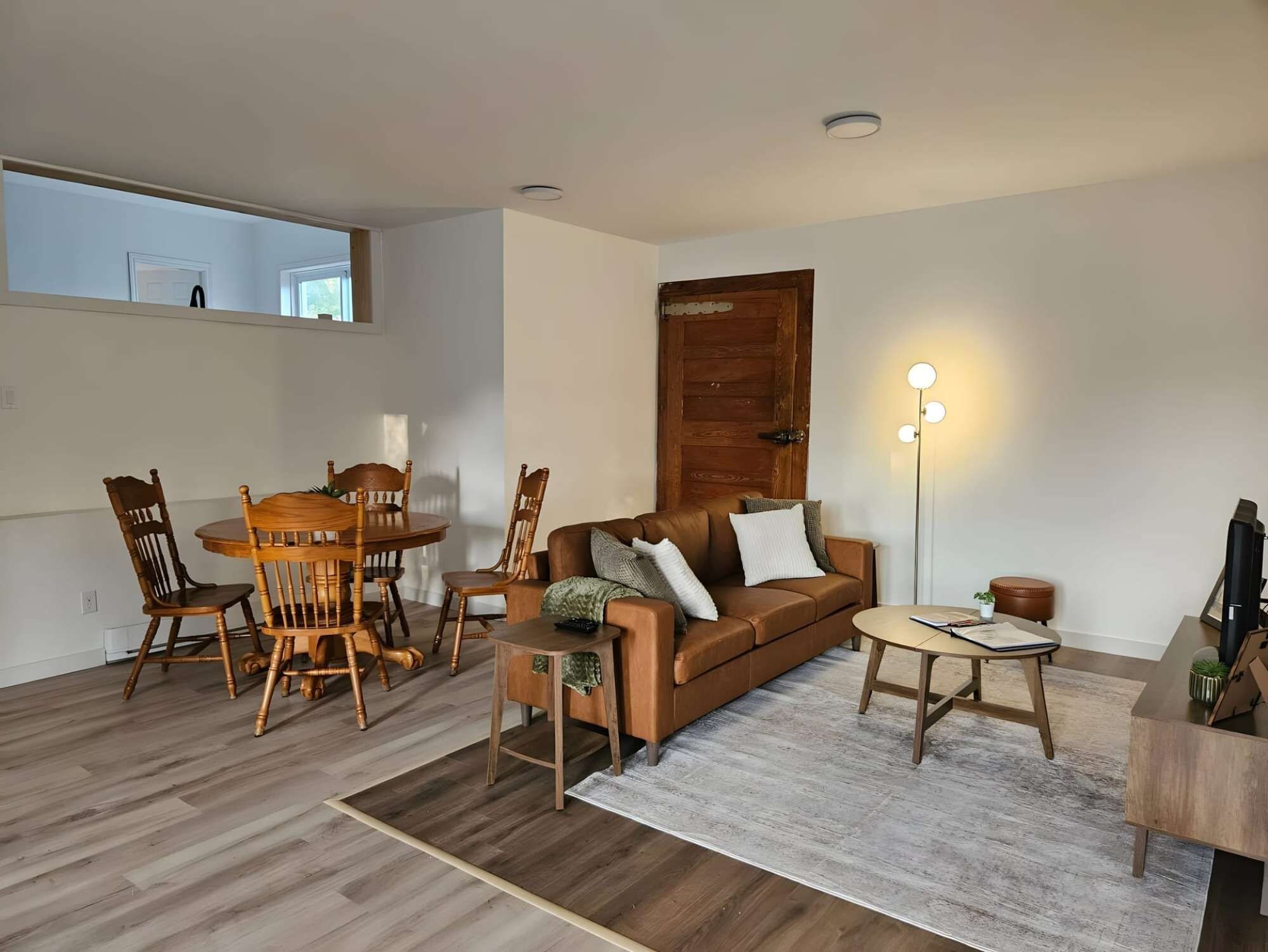 A living room with a wooden dining table, chairs, a sofa, a coffee table, and a floor lamp.
