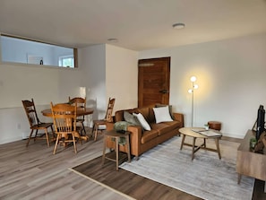 A living room with a wooden dining table, chairs, a sofa, a coffee table, and a floor lamp.