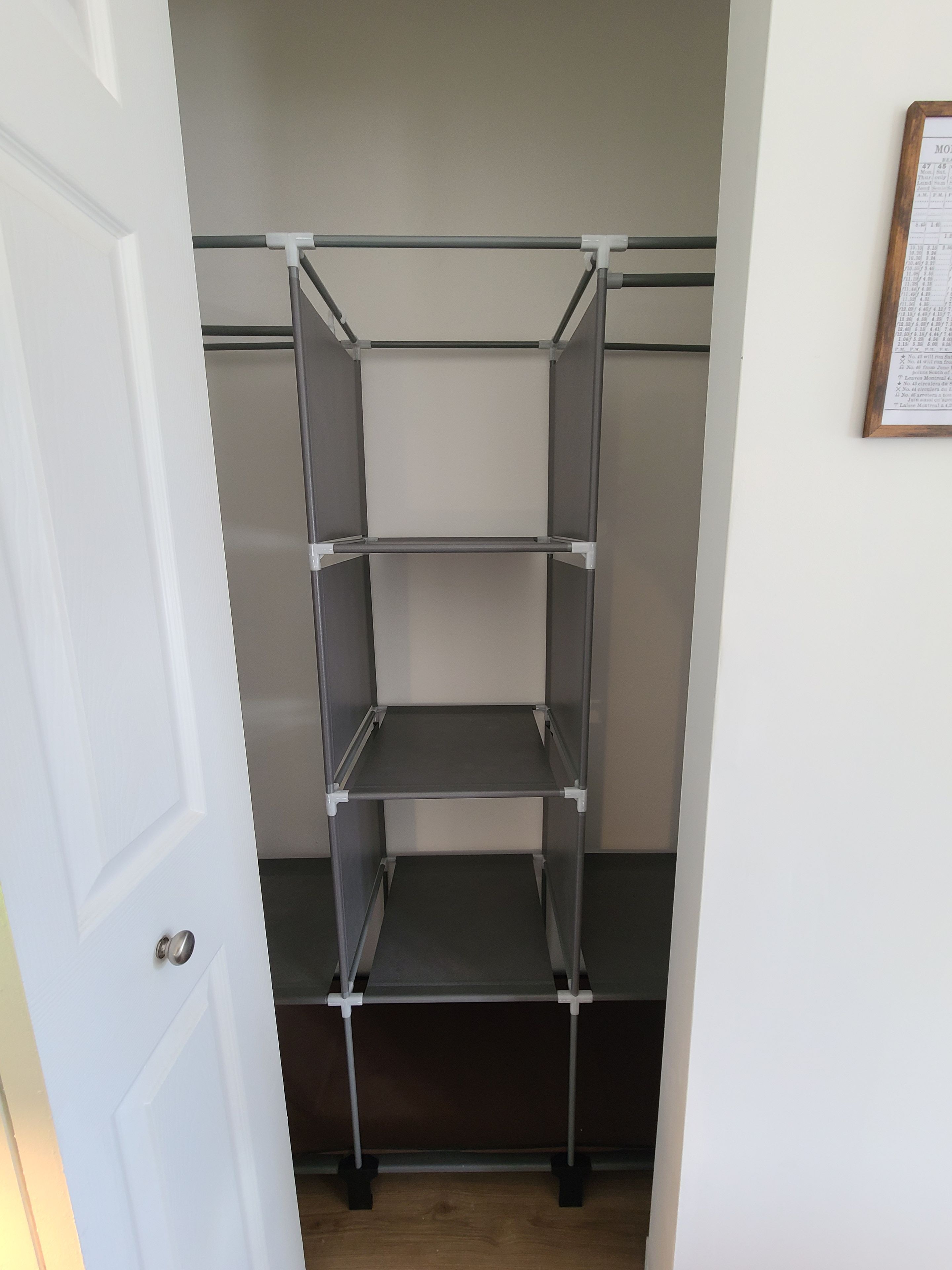 Uma estante de metal num quarto com uma porta branca e um documento emoldurado na parede.