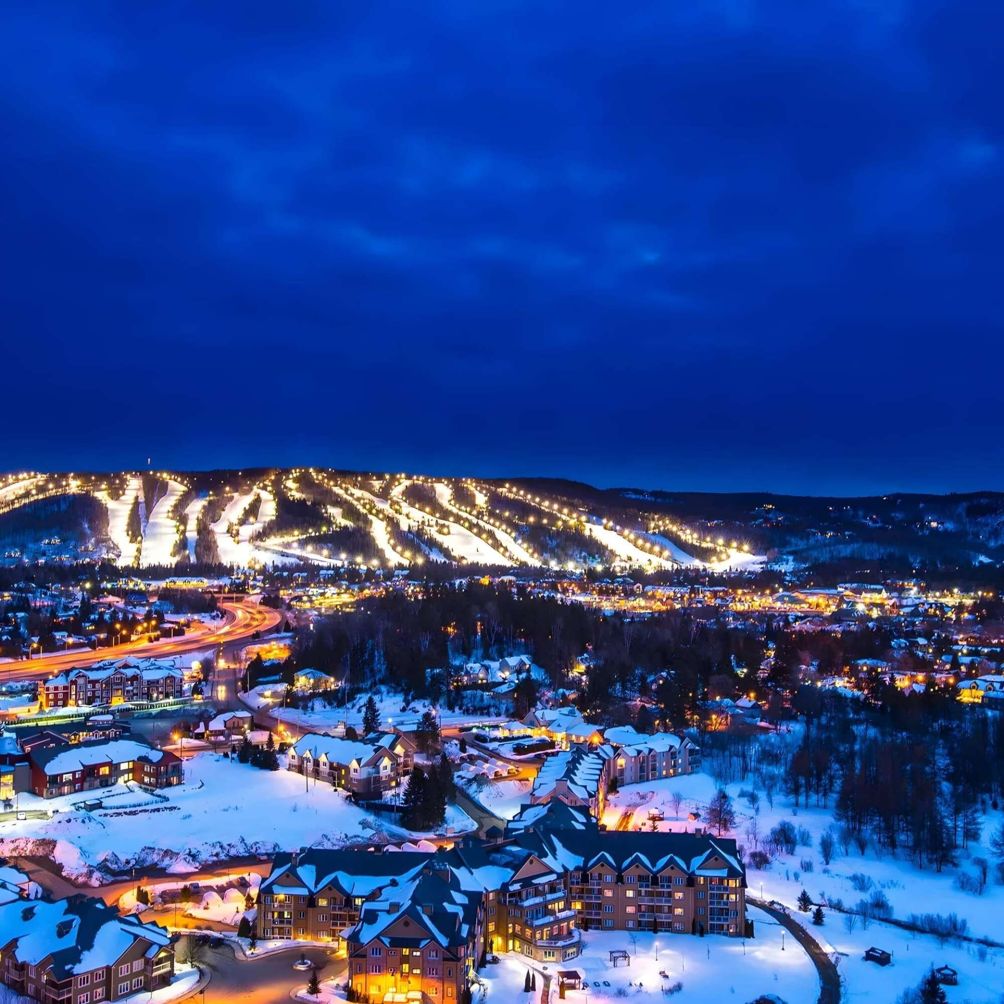 Une ville enneigée la nuit, avec des bâtiments illuminés et des routes sinueuses.