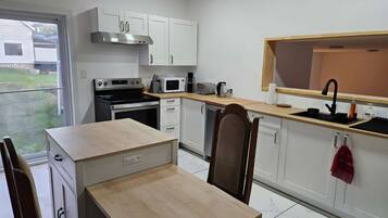Cocina compacta con horno integrado, microondas y cafetera, comedor con mesa y sillas, y ventana con vista a un jardín.