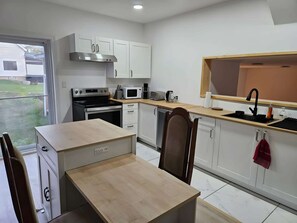 A compact kitchen with a built-in oven, microwave, and coffee maker, a dining area with a table and chairs, and a window overlooking a yard. - Historic house – Skiing, hiking, relaxation, and nature (Montcalm)