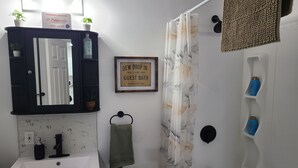 Baño con lavamanos, espejo, toallero, cortina de ducha y artículos de aseo.