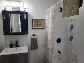 Een badkamer met een wastafel, spiegel, handdoekhouder, douchegordijn en toiletartikelen.