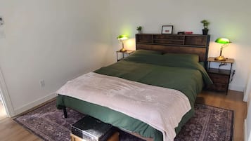 A bedroom with a bed, two bedside tables, a nightstand, a small wooden chest, and a patterned rug.