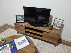 Un televisor de pantalla plana sobre un mueble de madera con dos fotografías enmarcadas y una planta pequeña.