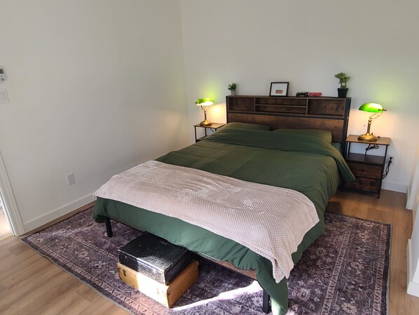 Un dormitorio con cama, lámparas de noche, mesita de noche, cómoda, alfombra y una planta pequeña.